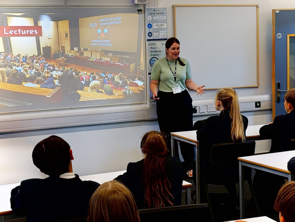 This picture shows a classroom setting with a female teacher or lecturer at the front, actively addressing a group of students.