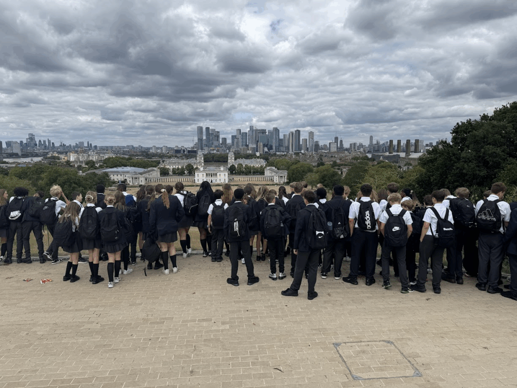 A Group of students in school uniform look out from a hill across to the city of London