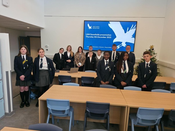 A group of students and adults posing in a classroom with a screen displaying "LAM Snowfields presentation."