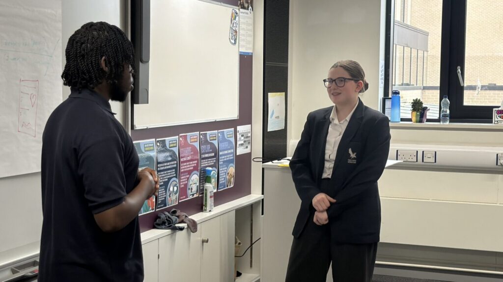 Student in black blazer and glasses talking to man in navy polo top